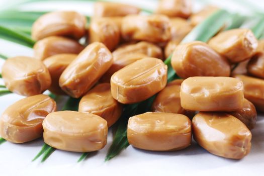 A detailed shot of smooth, homemade caramel candies on green leaves, showcasing a delicious dessert.