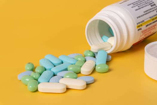 Open bottle of assorted pills spilling onto a vibrant yellow background.