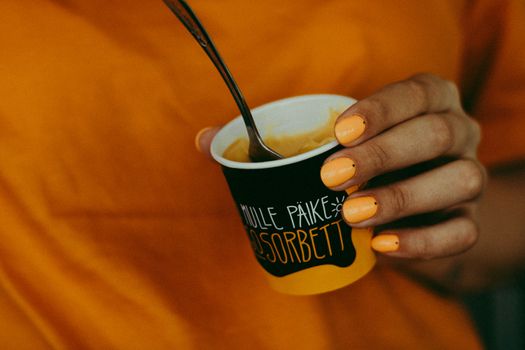Close-up of a hand holding refreshing mango sorbet with orange nails.