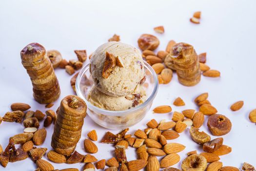 Scoops of almond fig ice cream in a glass bowl surrounded by almonds and figs.
