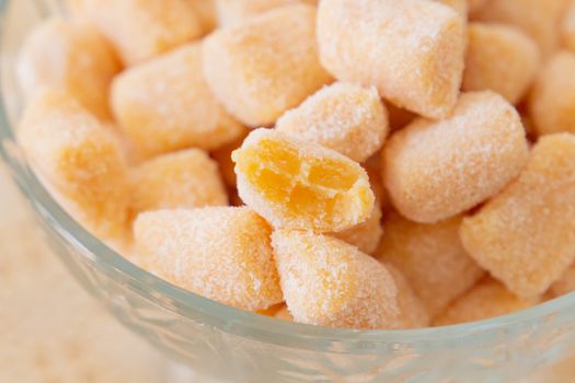 Close-up of sugar-coated passion fruit candies in a glass bowl, showcasing vibrant yellow hue.