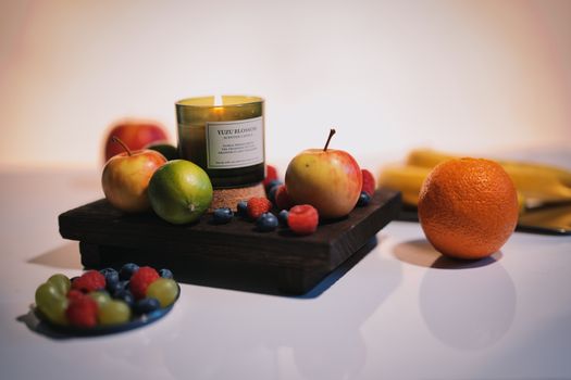 Vibrant fruits and a lit Yuzu Blossom candle create a cozy still life.