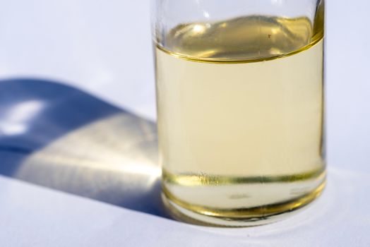 A close-up image of a glass bottle with liquid, showcasing light reflection and shadow on a white surface.