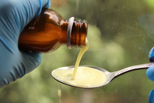 A gloved hand pours liquid medication from a brown bottle into a spoon.