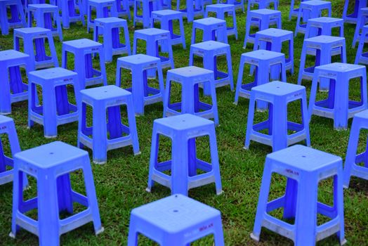 A pattern of vibrant blue plastic stools arranged orderly on green grass outdoors, creating a striking visual contrast.