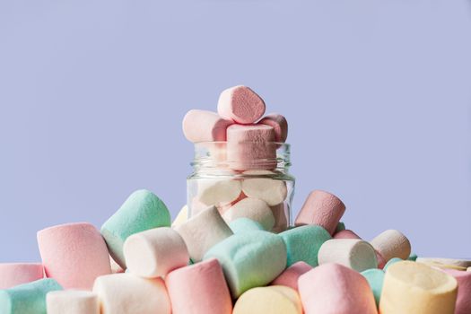 A vibrant collection of colorful marshmallows in a glass jar on a light background.