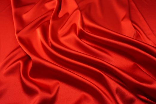 Close-up of smooth, red silk fabric with elegant ripples, highlighting its texture and shine.
