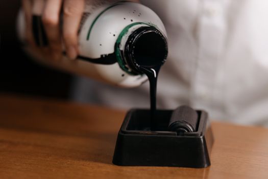 A close-up image of ink from a bottle being poured onto a roller, highlighting art supplies.