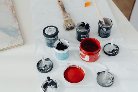Assorted paint cans and brushes arranged on a white surface, perfect for artistic projects.