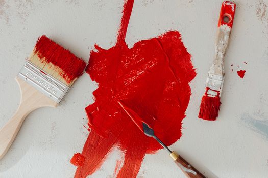 Close-up of red paintbrushes and palette knife on a white surface with bright red paint.