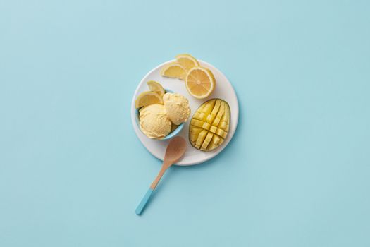 Top view of lemon and mango ice cream with sliced fruit on a blue background.
