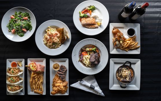 Top view of elegantly plated restaurant dishes paired with wine bottles, showcasing diverse cuisine.