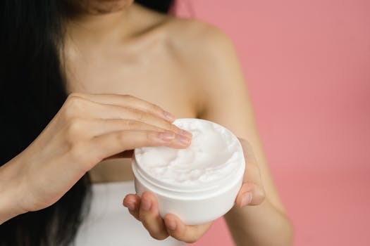 Sodium Bicar Close-up of a woman applying white cream from a jar against a pink background.